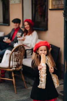 A stylish girl with baguettes stands near the store against the background of her parents.