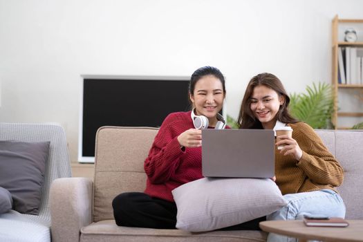 Two asian young woman happy smiling and using computer laptop on couch in living room at home.