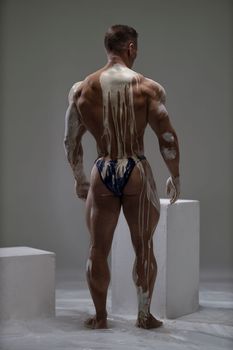 A strong man demonstrates a muscular relief back covered with white clay. Ideal body with a low percentage of fat as a result of a hard sports routine