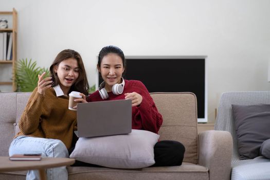 Two asian young woman happy smiling and using computer laptop on couch in living room at home.