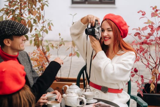 A stylish family of three is sitting at a table outside in a cafe and drinking coffee. Dad, mom and daughter in the autumn city.