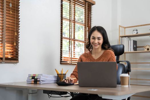 Asian indian Female director working in the office sitting at a desk analyzing business statistics holding diagrams and charts using a laptop computer,.