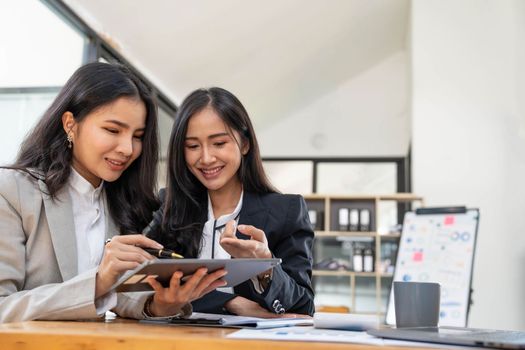 Two young Asian businesswoman discuss investment project working and planning strategy. Business people talking together with laptop computer at office..