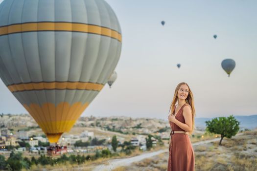 Tourist woman looking at hot air balloons in Cappadocia, Turkey. Happy Travel in Turkey concept. Woman on a mountain top enjoying wonderful view.