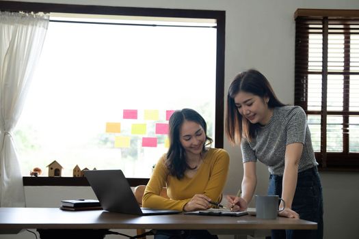 Two young Asian business woman talk, consult, discuss working with new startup project idea presentation analyze plan marketing and investment in the office...