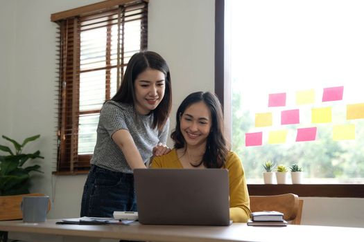 Two young Asian business woman talk, consult, discuss working with new startup project idea presentation analyze plan marketing and investment in the office...