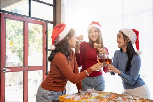 Group of Asian friends gather to celebrate Christmas with champagne and eating pizza at home. Joy of holiday party with friends or colleague concept.