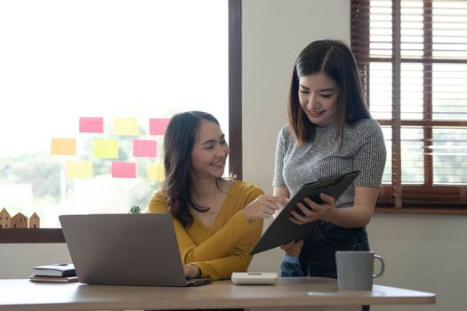 Two young Asian business woman talk, consult, discuss working with new startup project idea presentation analyze plan marketing and investment in the office...