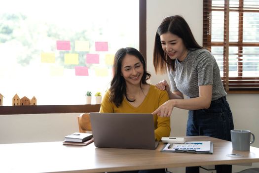 Two young Asian business woman talk, consult, discuss working with new startup project idea presentation analyze plan marketing and investment in the office...