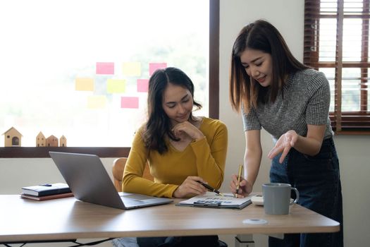 Two young Asian business woman talk, consult, discuss working with new startup project idea presentation analyze plan marketing and investment in the office...