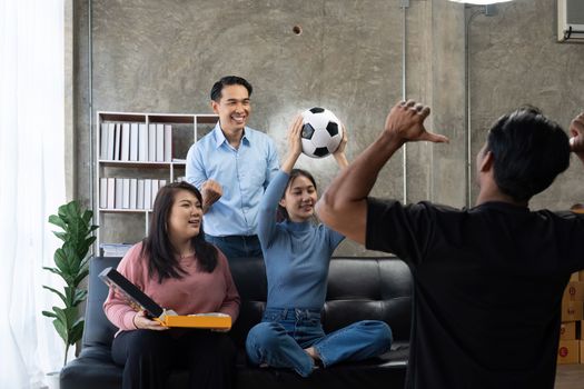 Friends watch sports on TV, cheer and celebrate. Happy diverse asian friend supporters fans sit on couch with popcorn and drinks.