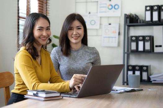 Two young Asian business woman talk, consult, discuss working with new startup project idea presentation analyze plan marketing and investment in the office...