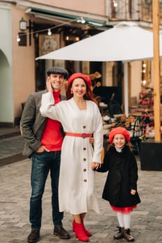 A stylish family of three strolls through the autumn city posing for a photographer . Dad, mom and daughter in the autumn city.