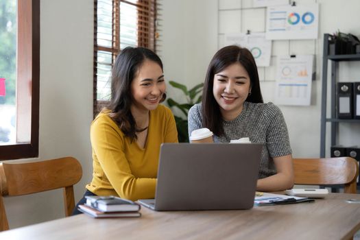 Two young Asian business woman talk, consult, discuss working with new startup project idea presentation analyze plan marketing and investment in the office..