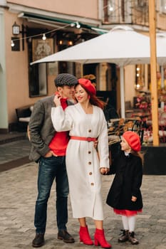 A stylish family of three strolls through the autumn city posing for a photographer . Dad, mom and daughter in the autumn city.