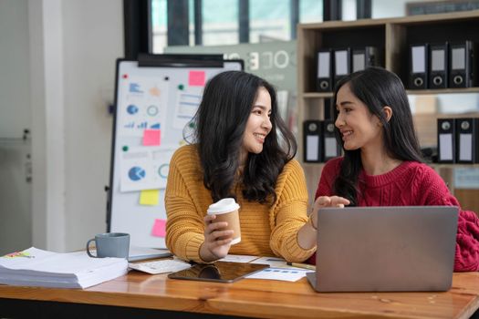 Two young Asian business woman talk, consult, discuss working with new startup project idea presentation analyze plan marketing and investment in the office..