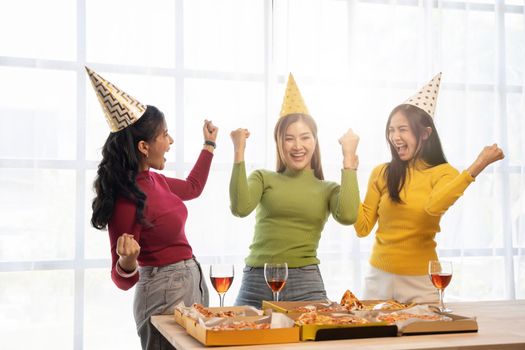 Group of Asian friends gather to celebrate Christmas with champagne and eating pizza at home. Joy of holiday party with friends or colleague concept.