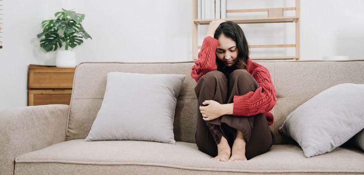 Depressed lonely unhappy mental woman sitting alone on the sofa at home with hand on face feel stress sad and worried disappointment