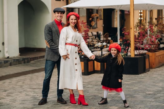 A stylish family of three strolls through the autumn city posing for a photographer . Dad, mom and daughter in the autumn city.