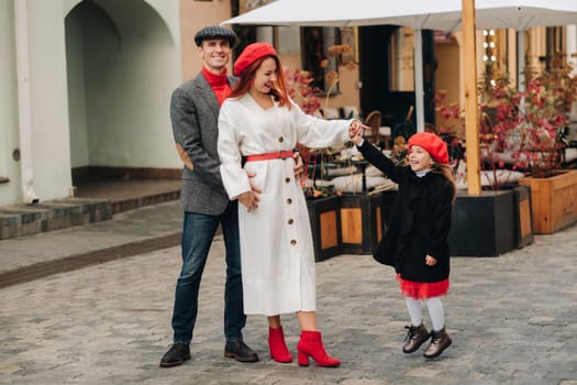 A stylish family of three strolls through the autumn city posing for a photographer . Dad, mom and daughter in the autumn city.