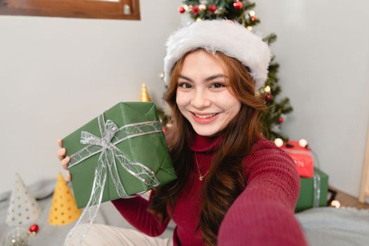 Selfie photo portrait of young girl take shot hold giftbox demonstrating her comfy house apartment christmas tree with decorations staying indoors.