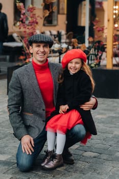 Portrait of a father and daughter sitting on a knee and being on a city street in autumn.