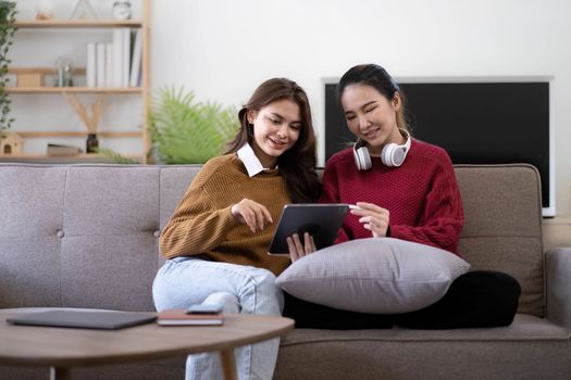 Two asian young woman happy smiling and using computer laptop on couch in living room at home.
