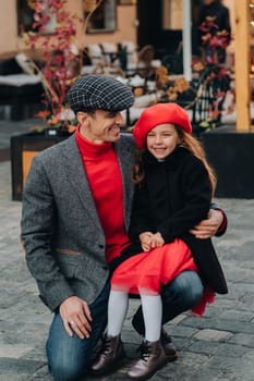 Portrait of a father and daughter sitting on a knee and being on a city street in autumn.