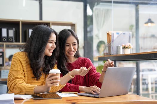 Two young Asian business woman talk, consult, discuss working with new startup project idea presentation analyze plan marketing and investment in the office..