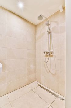 Shower faucets attached to tiled wall near glass partition and ornamental curtail in washroom at home