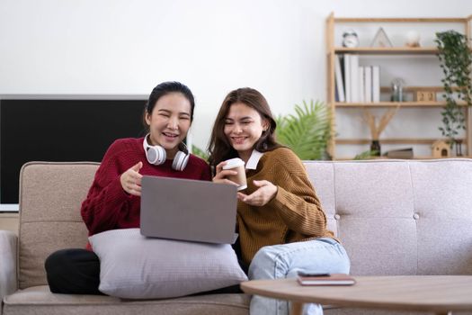 Two asian young woman happy smiling and using computer laptop on couch in living room at home.