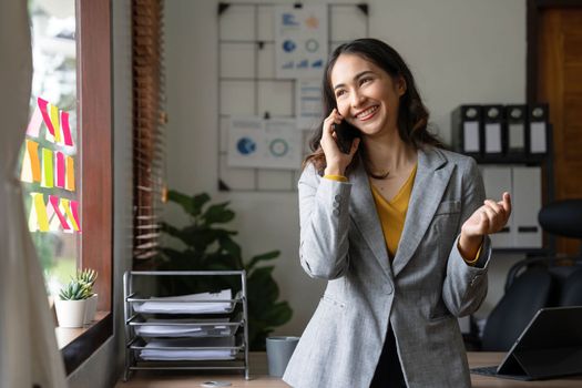 Smiling beautiful Asian businesswoman analyzing chart and graph showing changes on the market and holding smartphone at office..