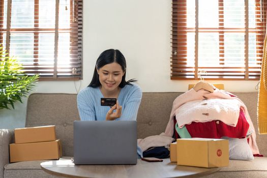 Young woman holding credit card for shopping online with computer while sitting in the living room at home. black friday concept