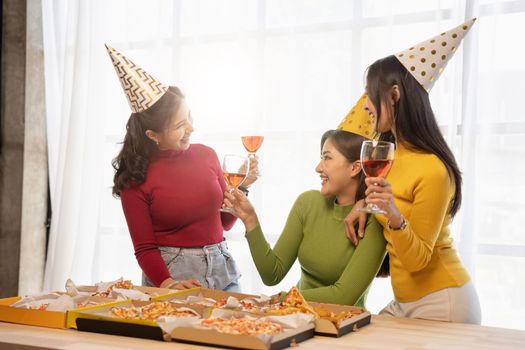Group of Asian friends gather to celebrate Christmas with champagne and eating pizza at home. Joy of holiday party with friends or colleague concept.