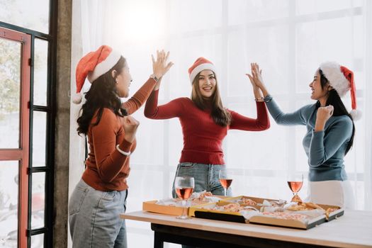 Group of Asian friends gather to celebrate Christmas with champagne and eating pizza at home. Joy of holiday party with friends or colleague concept.