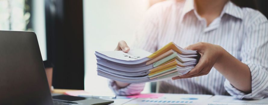 Business Documents concept : Employee woman hands working in Stacks paper files for searching and checking unfinished document achieves on folders papers at busy work desk office. Soft focus.