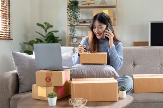 Small business entrepreneur SME freelance woman using phone call receive from customer checking product on stock at home office, online marketing packaging delivery box, SME e-commerce concept.