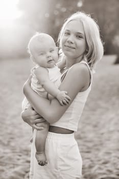 A mother holds a happy baby boy in her arms in a summer park.