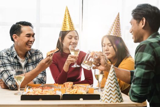 Group of diverse Asian friends gather to celebrate Christmas with champagne and eating pizza at home. Joy of holiday party with friends or colleague concept.