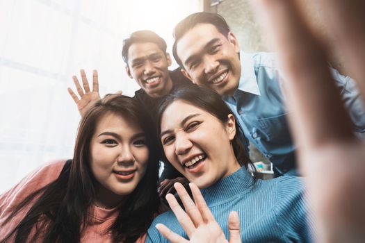 Friends watch sports on TV, cheer and celebrate. Happy diverse asian friend supporters fans sit on couch with popcorn and drinks. video call on mobile phone.