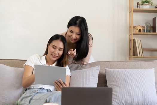 Two young asian girls are sitting on couch using digital tablet at home.