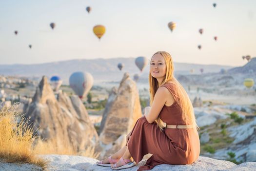 Tourist woman looking at hot air balloons in Cappadocia, Turkey. Happy Travel in Turkey concept. Woman on a mountain top enjoying wonderful view.