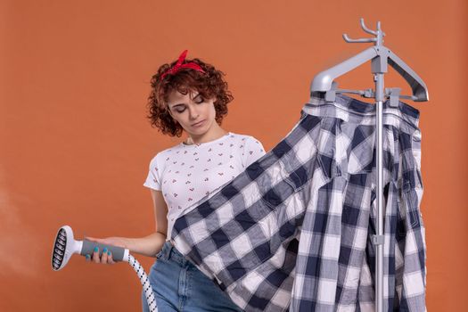 A woman is pondering and bubbling while ironing her shirt. Ironing steamer. Attractive girl with dark and curly hair. Hot steam.