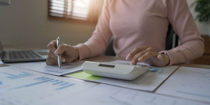 Close up woman or accountant hand working on calculator to calculate business data, accounting document and laptop computer at home.