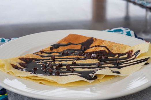 Pancake crepe a la carte dessert meal with chocolate sauce and chunks on white plate 