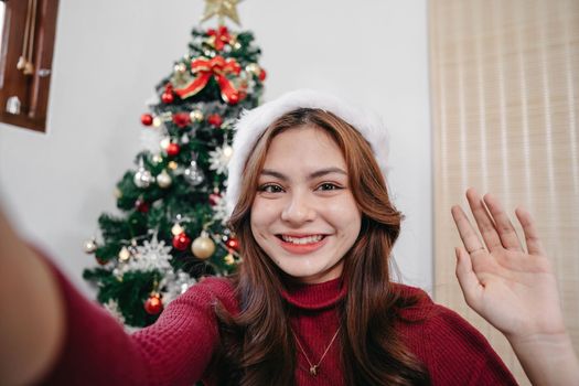 Portrait young woman using video call talking with friend or boyfriend. Christmas tree decorated with ornament in living room at home. Christmas and New Year holiday festival.