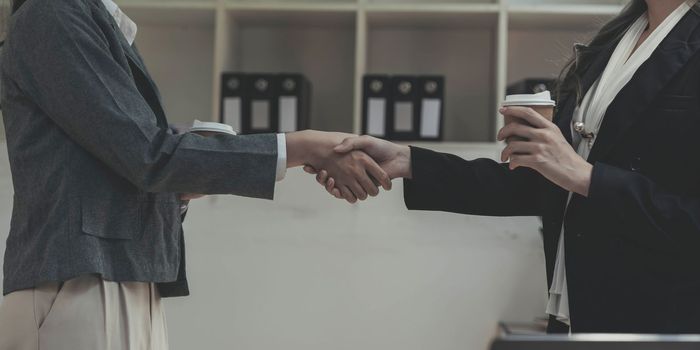 Two Asian businesswomen are shaking hands in the office. business cooperation, business dealing, Congratulations, greeting. close-up hands image.
