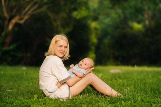 A mother holds a happy baby boy in her arms in a summer park.