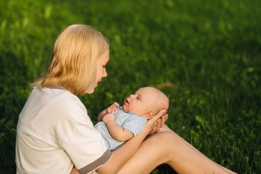 A mother holds a happy baby boy in her arms in a summer park.