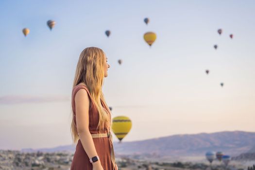 Tourist woman looking at hot air balloons in Cappadocia, Turkey. Happy Travel in Turkey concept. Woman on a mountain top enjoying wonderful view.